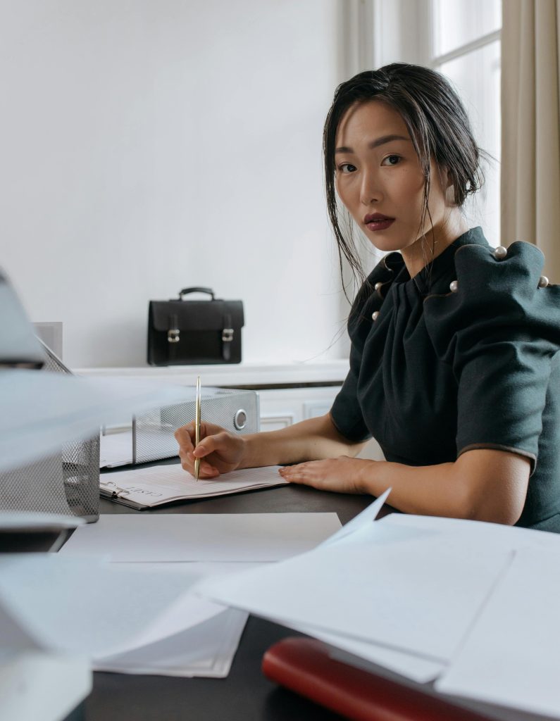 Asian woman writing at desk - BAM Group (business funding advisory)